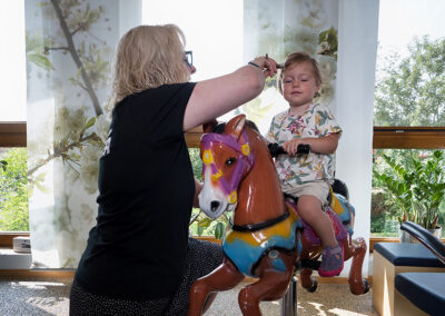 Kleinkind bekommt von einer Frisörin auf einem Karusellpferd die Haare geschnitten